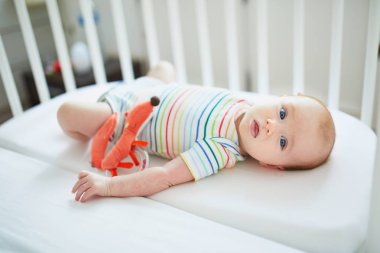 Bebek kız oyuncakla yatakta yatıyordu. Güneşli odasında oynayan küçük çocuk