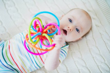 Bebek kız oyuncakla yatakta yatıyordu. Güneşli odasında oynayan küçük çocuk