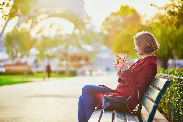 色鮮やかな紅葉の秋の日にパリのエッフェル塔近くのベンチに座っているの束と美しい若いフランス人女性 — ストック写真