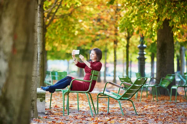 美丽的年轻女子在巴黎的杜乐丽花园 在一个明亮的秋季一天 采取自拍与她的手机 法国秋季旅游与度假 — 图库照片