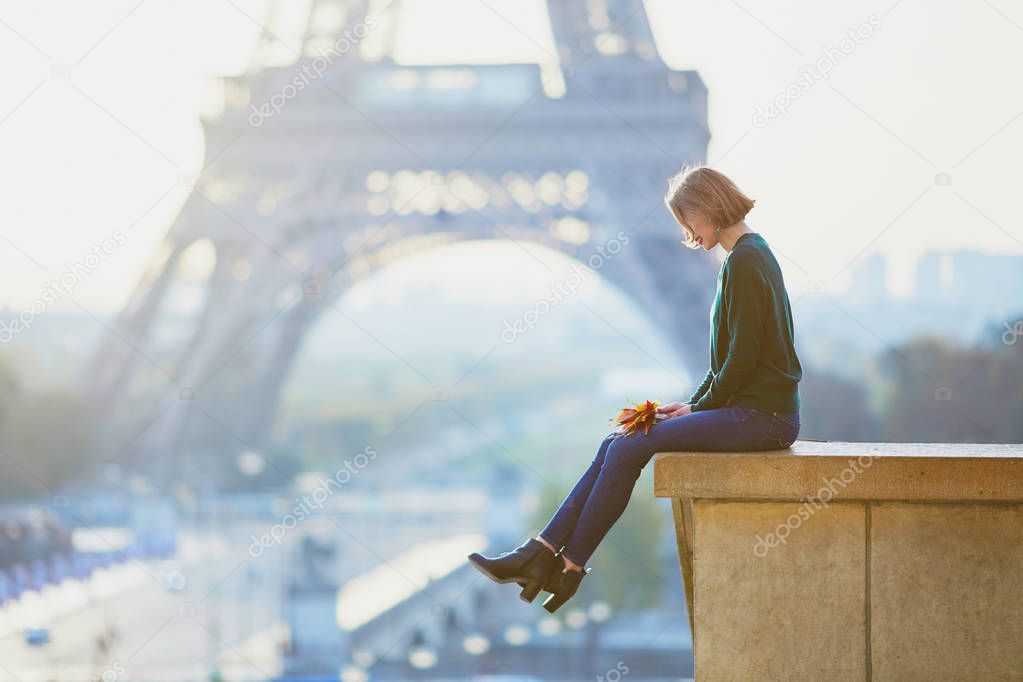 Beautiful young French woman with bunch of colorful autumn leaves near the Eiffel tower in Paris on a fall day