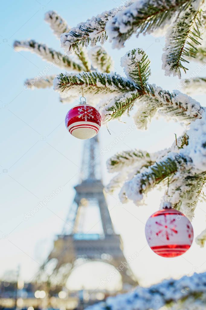 Christmas tree covered with snow and decorated with red toys near the Eiffel tower in Paris, France