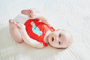 Sırtüstü yatıp ayaklarına dokunan tatlı bir kız çocuğu. Mutlu sağlıklı çocuk evde, kreşte.