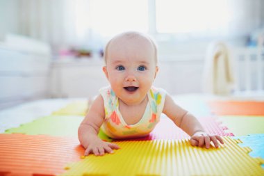 Sevimli bir kız bebek renkli oyun hasırında göbek yapıyor. Mutlu sağlıklı çocuk yerde oynuyor.