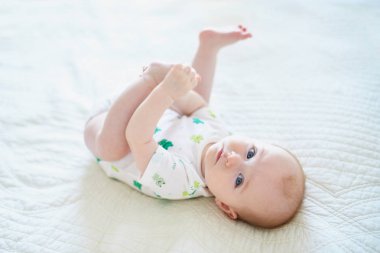 Sırtüstü yatıp ayaklarına dokunan tatlı bir kız çocuğu. Mutlu sağlıklı çocuk evde, kreşte.