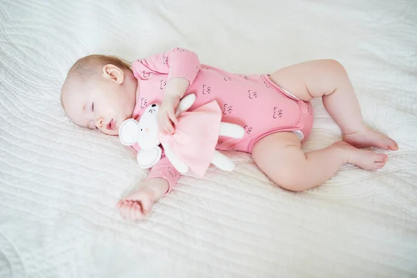 Baby girl having a nap with her favorite mouse toy. Little child sleeping on bed with comforter. Infant kid in sunny nursery