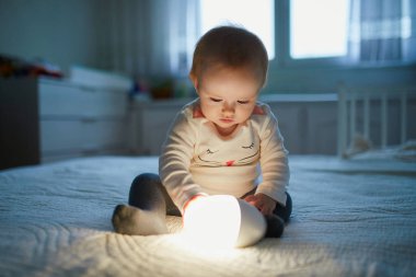 Bebek odasında başucunda lambayla oynayan sevimli bir kız. Gece lambasıyla yatakta oturan mutlu çocuk. Küçük çocuk uyumadan önce akşam evde.