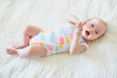 Sevimli bebek yatakta uzanıp gülümsüyor. Mutlu sağlıklı küçük çocuk gülüyor. Güneşli kreşte küçük bir çocuk.