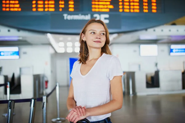 彼女のフライトを待っている案内板の近くの荷物を空港で若い女性 — ストック写真