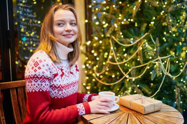 Kafede kahve veya sıcak çikolata içme tatil kazaklı neşeli genç kız Noel ve çıkartıyorum Noel hediyesi için dekore edilmiş