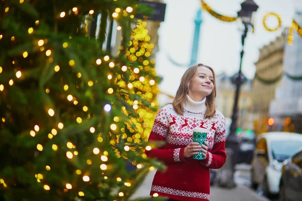 パリの路上で移動するホットド リンクと歩いて休日のセーターで幸せな若い女の子がクリスマスの装飾 — ストック写真