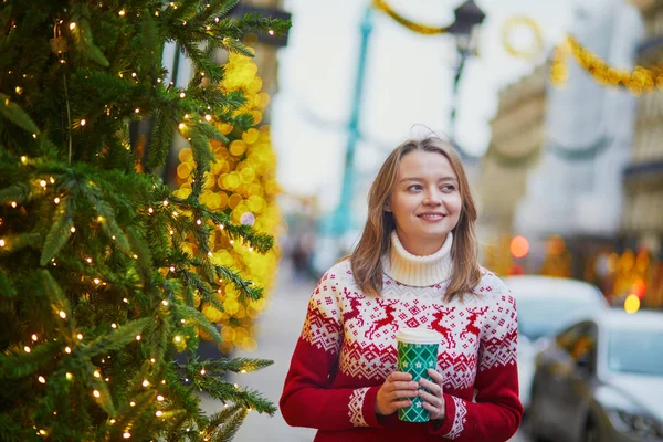 パリの路上で移動するホットド リンクと歩いて休日のセーターで幸せな若い女の子がクリスマスの装飾 — ストック写真