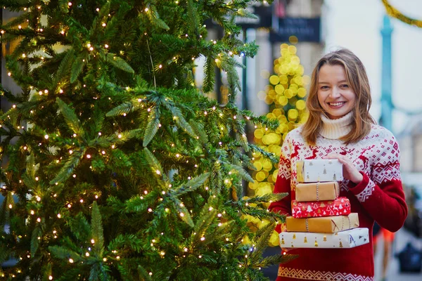 愉快的年轻女孩在假日毛衣与一堆假日礼物在巴黎装饰圣诞节街道 — 图库照片