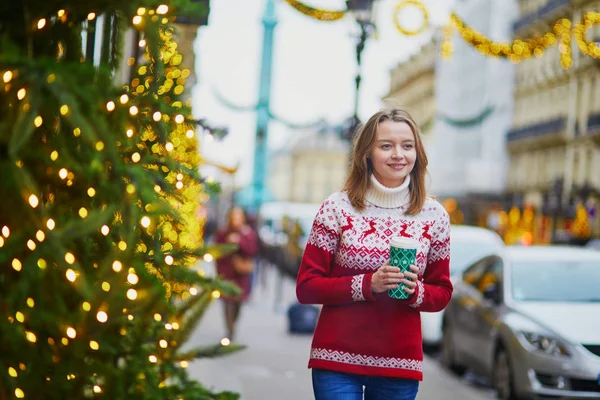 パリの路上で移動するホットド リンクと歩いて休日のセーターで幸せな若い女の子がクリスマスの装飾 — ストック写真