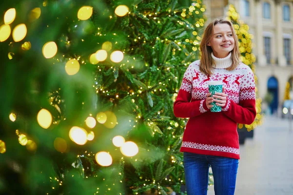 パリの路上で移動するホットド リンクと歩いて休日のセーターで幸せな若い女の子がクリスマスの装飾 — ストック写真