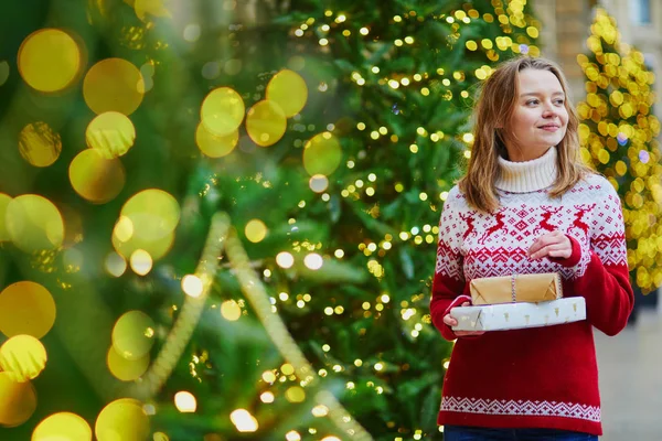 パリの街でクリスマス プレゼントの山で休日のセーターで幸せな若い女の子がクリスマスの装飾 — ストック写真