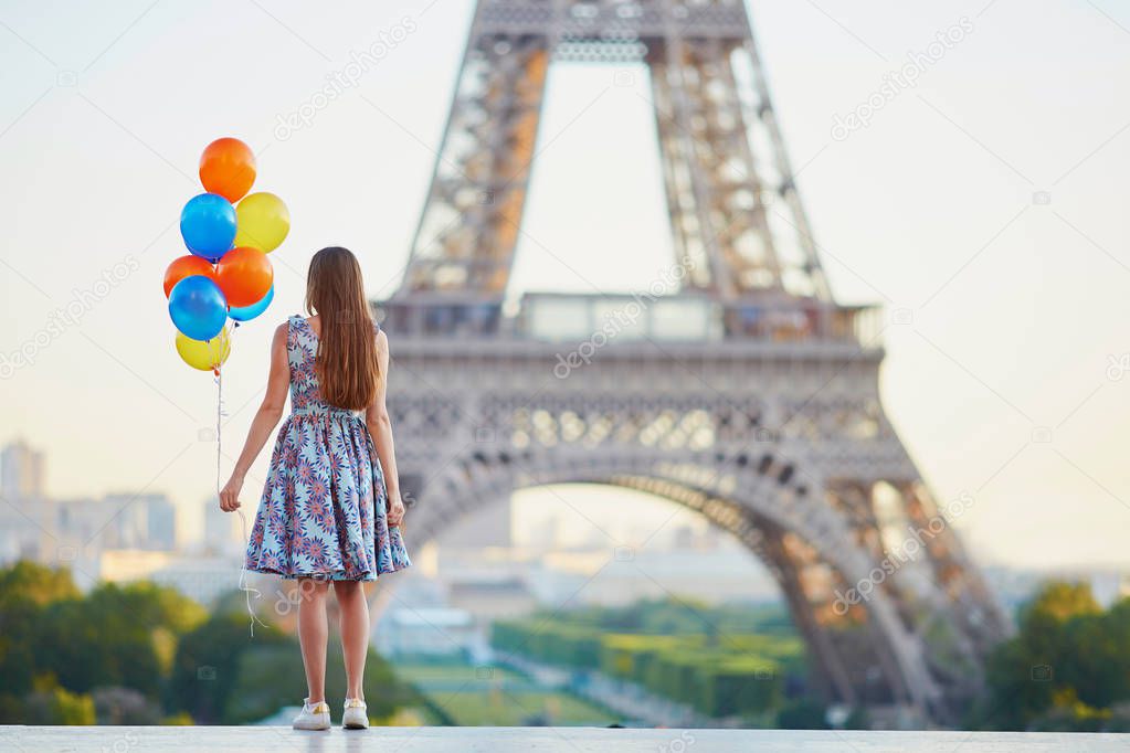 Romantic young woman in Paris with bunch of colorful balloons looking at the Eiffel tower