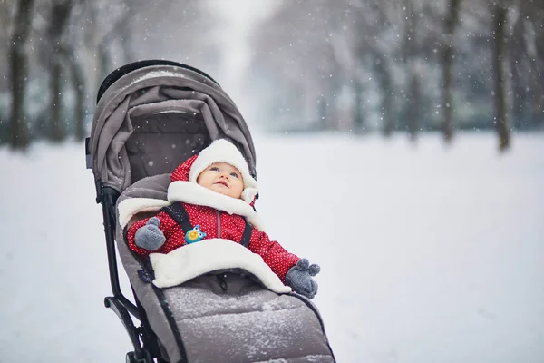 Happy smiling baby girl in stroller in Paris day with heavy snow. Little kid enjoying the very first snow. Unusual weather conditions in France.
