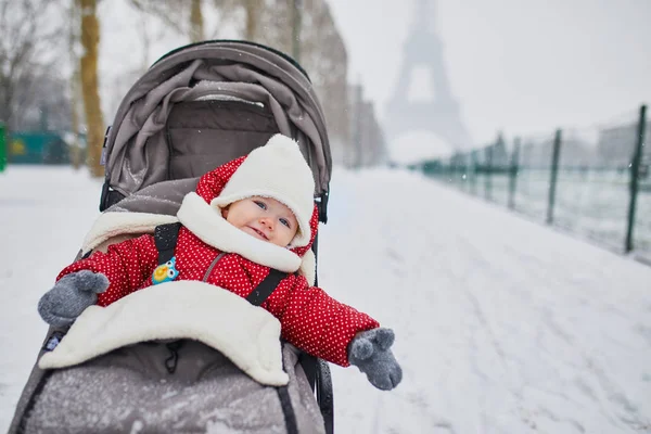 大雪の日にエッフェル塔近くのベビーカーで幸せな笑みを浮かべて赤ちゃん女の子 小さな子供は 非常に最初の雪を楽しみます パリの異常気象条件 — ストック写真