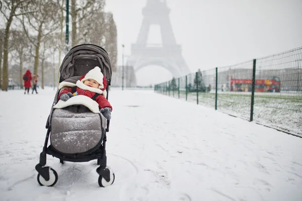 大雪の日にエッフェル塔近くのベビーカーで幸せな笑みを浮かべて赤ちゃん女の子 小さな子供は 非常に最初の雪を楽しみます パリの異常気象条件 — ストック写真