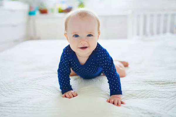 小女孩爬到床上笑着 穿着蓝色衣服的健康的小孩快乐 在阳光灿烂的托儿所里的婴儿 — 图库照片
