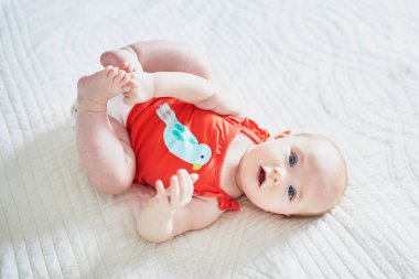 Sırtüstü yatıp ayaklarına dokunan tatlı bir kız çocuğu. Kreşteki sağlıklı çocuk.