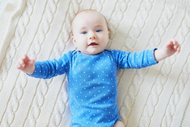 Sevimli bebek yatakta uzanıp gülümsüyor. Mutlu sağlıklı küçük çocuk gülüyor. Güneşli kreşte küçük bir çocuk.