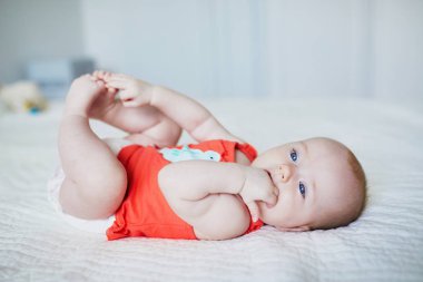 Sırtüstü yatıp ayaklarına dokunan tatlı bir kız çocuğu. Kreşteki sağlıklı çocuk.
