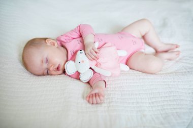 Küçük kız en sevdiği fare oyuncağıyla kestiriyor. Küçük çocuk yorganla yatakta uyuyor. Uyku eğitimi konsepti. Güneşli kreşte küçük bir çocuk.