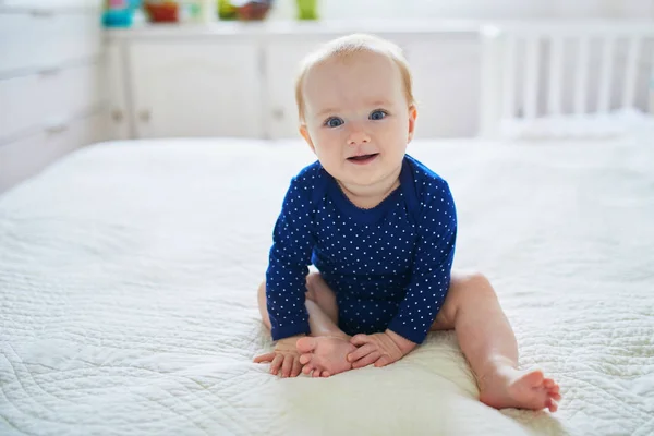 小女孩坐在床上笑着 穿着蓝色衣服的健康的小孩快乐 在阳光灿烂的托儿所里的婴儿 — 图库照片
