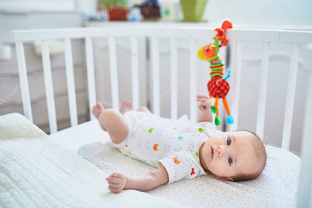 Adorable baby girl lying in the crib. Little child having a day nap in cot. Infant kid resting and playing with toys in nursery