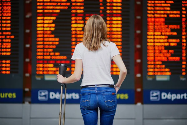 フライト情報ディスプレイ近くに移動する荷物とコーヒーの国際空港で若い女性 — ストック写真