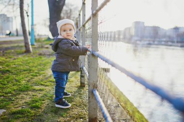 Bir yaşında kız parkta metal çit yanında ayakta. Yürümeyi öğrenen yürümeye başlayan çocuk. Çok güzel çocuk Paris, Fransa'da yürüyüş
