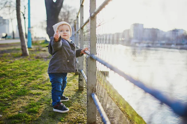 一个一岁的女孩站在公园的金属栅栏旁边 用手指指着 幼儿学习走路 可爱的孩子走在巴黎 — 图库照片