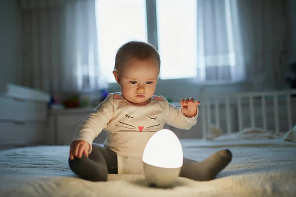 Adorable niña jugando con la lámpara de noche en el vivero —  Fotos de Stock