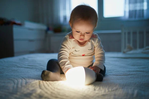 Очаровательная девочка играет с прикроватной лампой в детской — стоковое фото