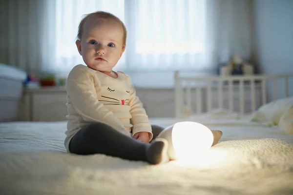 Adorable niña jugando con la lámpara de noche en el vivero —  Fotos de Stock