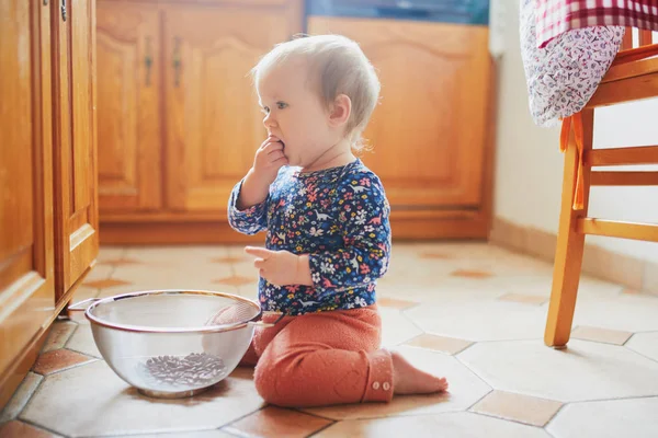 Девочка, сидящая на полу на кухне и играющая с посудой — стоковое фото