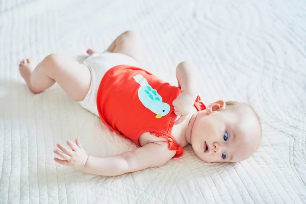 Schattig baby meisje liggend op haar rug op bed — Stockfoto