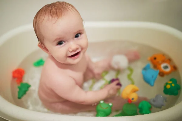 Menina bonito brincando com brinquedos de borracha em pequena banheira — Fotografia de Stock