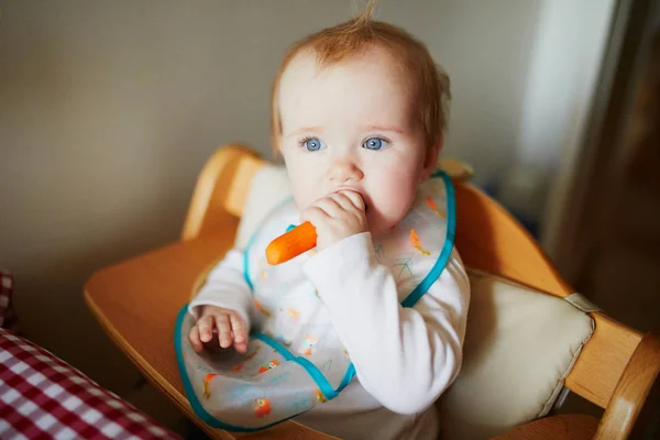 Menina bonito comer cenoura na cozinha — Fotografia de Stock