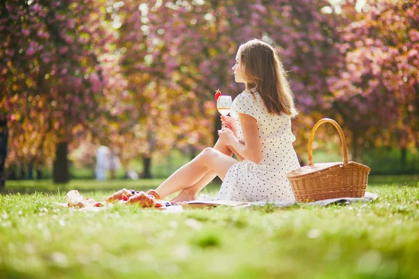 Mulher fazendo piquenique no dia ensolarado da primavera no parque durante a temporada de flor de cereja — Fotografia de Stock