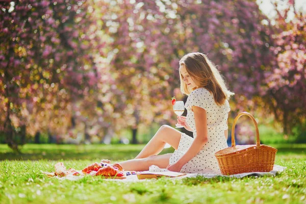 Mulher fazendo piquenique no dia ensolarado da primavera no parque durante a temporada de flor de cereja — Fotografia de Stock