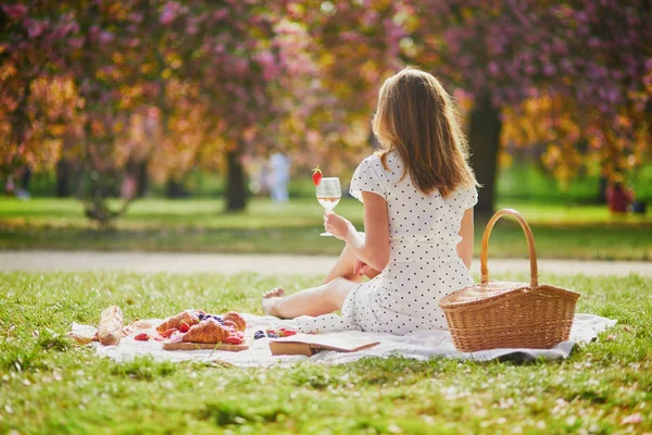 Woman having picnic on sunny spring day in park during cherry blossom season — Stockfoto