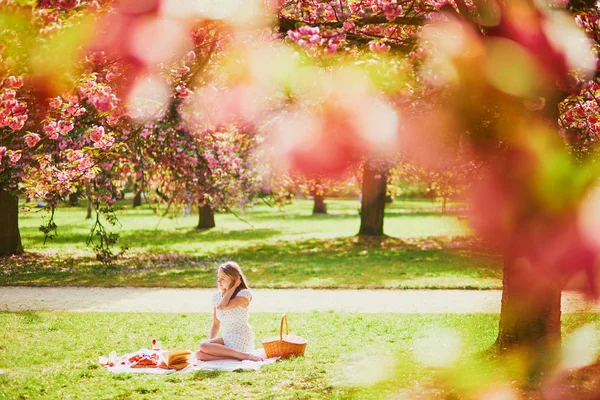 Mujer haciendo picnic en el soleado día de primavera en el parque durante la temporada de flores de cerezo —  Fotos de Stock