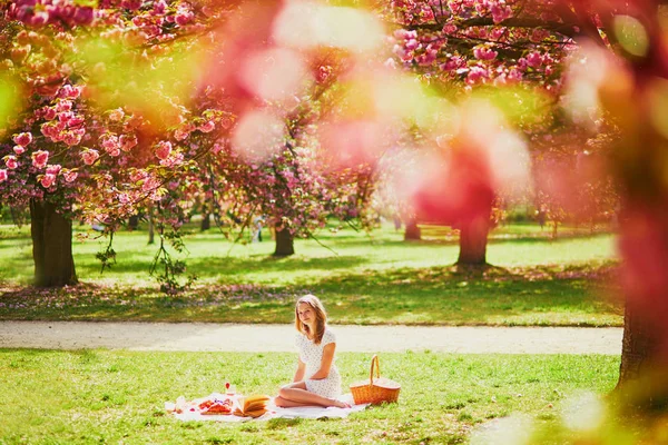 Mujer haciendo picnic en el soleado día de primavera en el parque durante la temporada de flores de cerezo — Foto de Stock