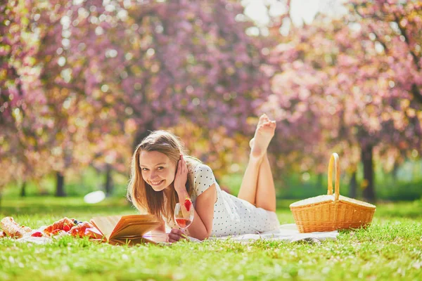 Woman having picnic on sunny spring day in park during cherry blossom season — Stockfoto
