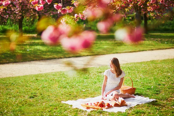 Woman having picnic on sunny spring day in park during cherry blossom season — Stock Photo, Image