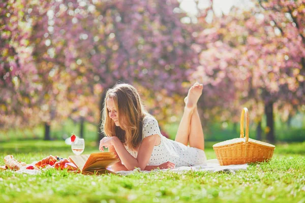 Güneşli bahar gününde parkta piknik yapan bir kadın. Kiraz çiçeği mevsiminde. — Stok fotoğraf