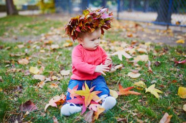 Kız çim üzerinde oturan ve renkli sonbahar yaprakları ile oynuyor